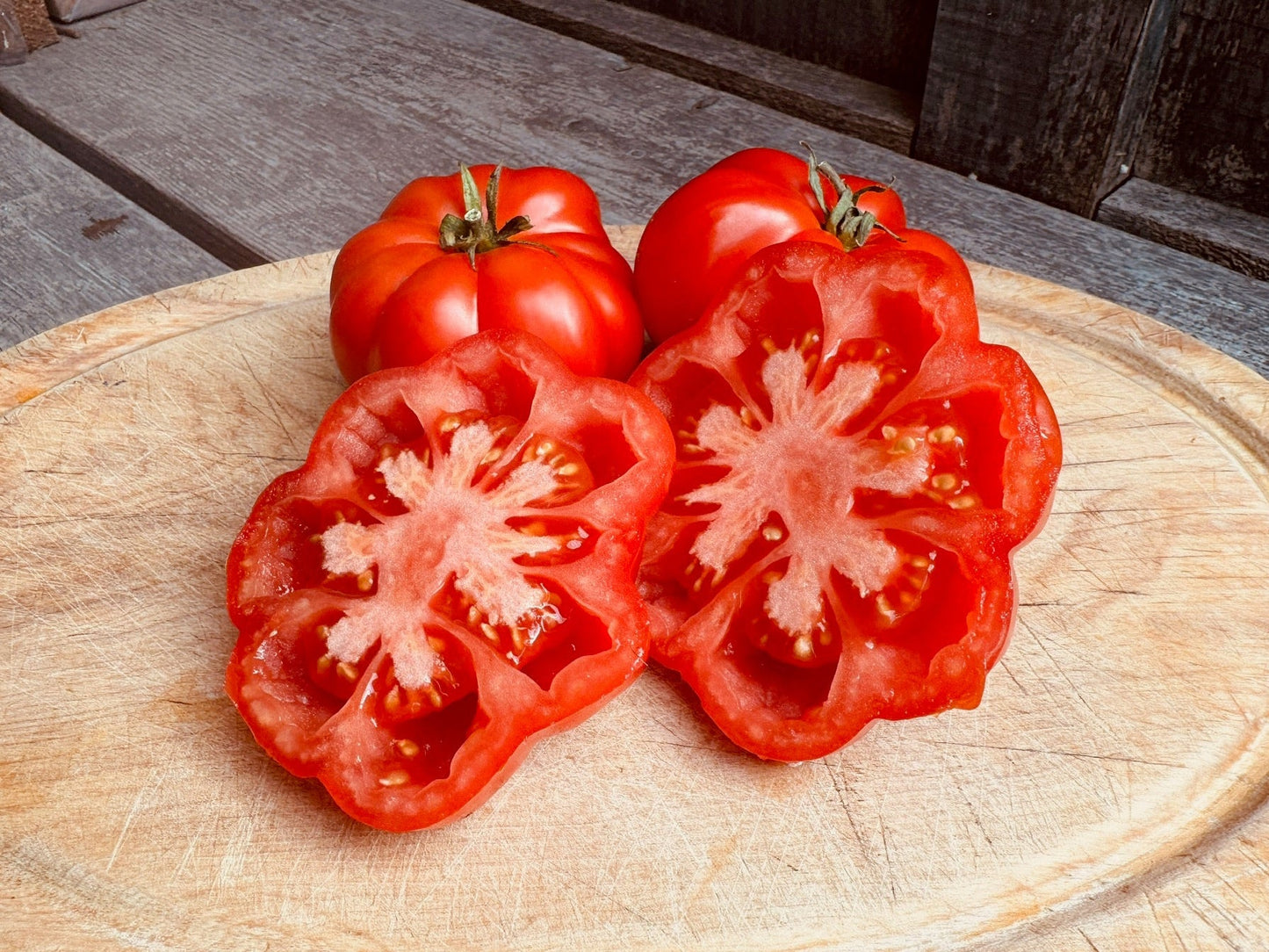 Tomatoes and a sliced tomato on a wooden cutting board
