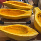 Sliced yellow squash on a wooden cutting board with a knife and other kitchen items.