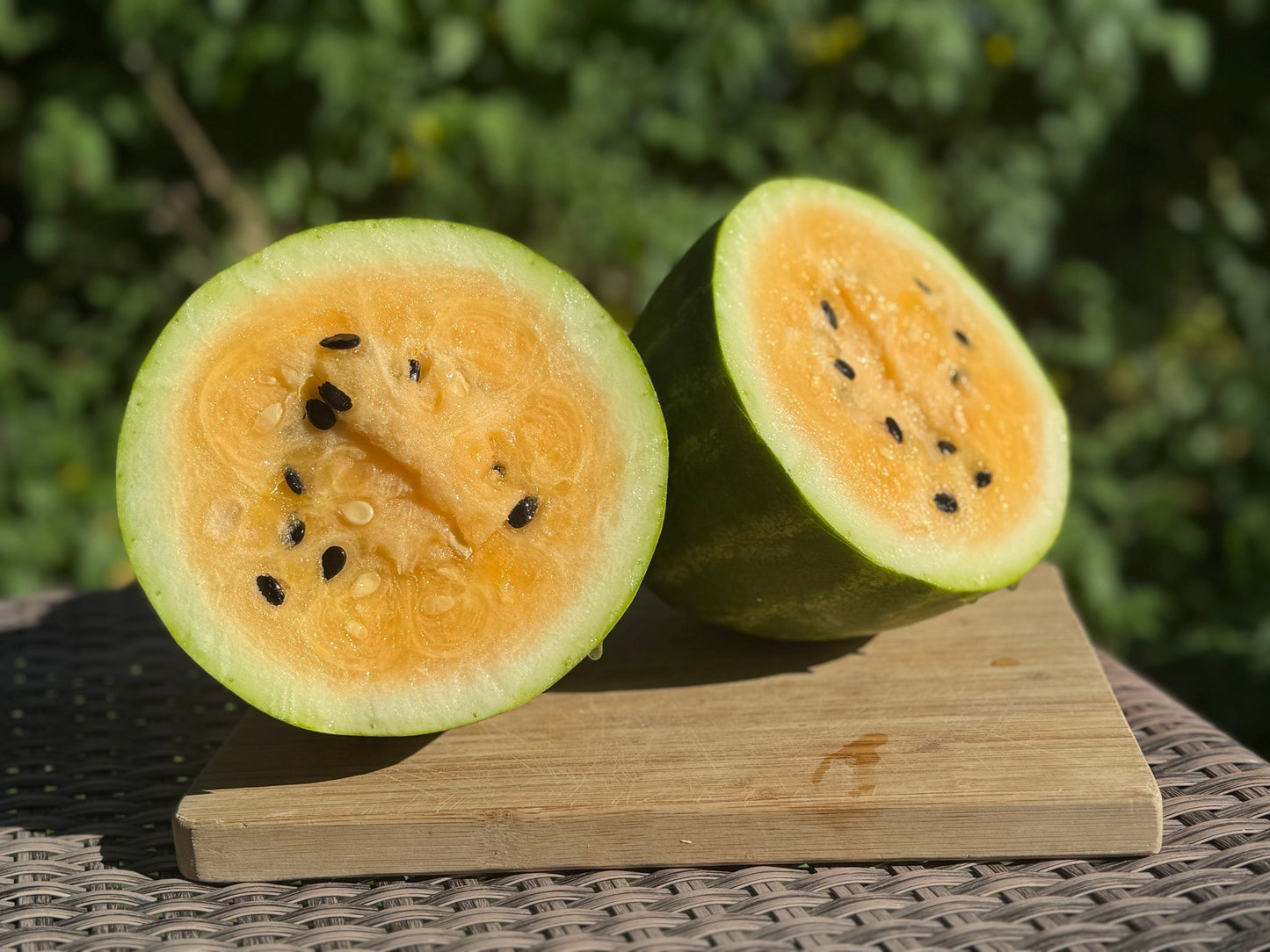Halved watermelon on a wooden board with a blurred green background